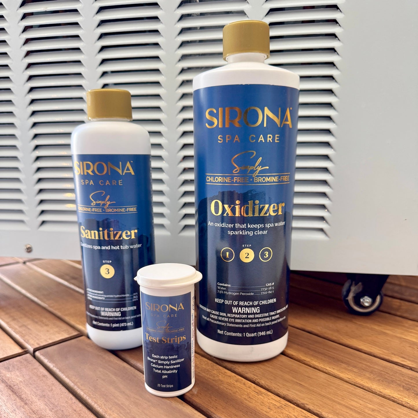 Three Sirona Spa Care products arranged on a wooden surface in front of a white slatted wall: a large Oxidizer bottle, a smaller Sanitizer bottle, and a smaller test strips container.